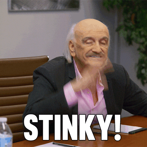 Older man in a blazer and pink shirt at a desk, winking/smugly smiling as his hand swishes by; captioned 'STINKY!' in bold white letters.